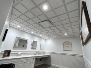 Modern bathroom with white cabinetry and drop ceiling installation featuring recessed lighting and wood-style flooring.
