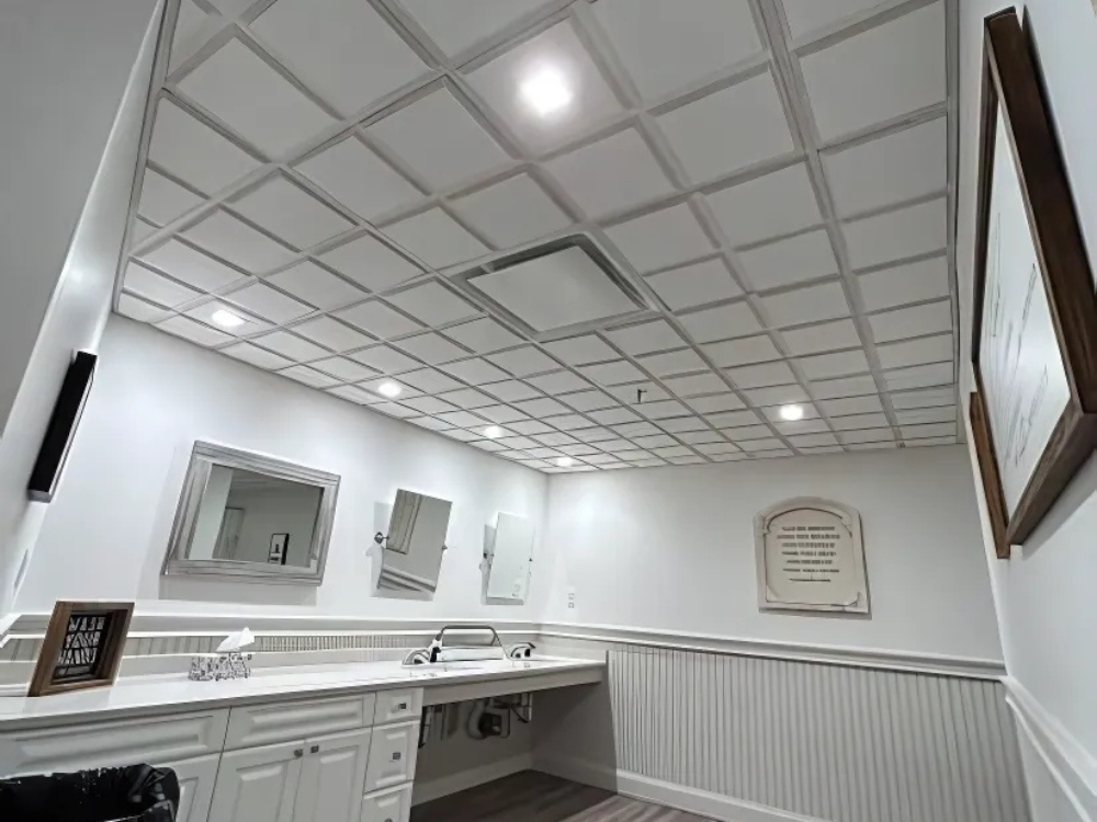 Modern bathroom with white cabinetry and drop ceiling installation featuring recessed lighting and wood-style flooring.