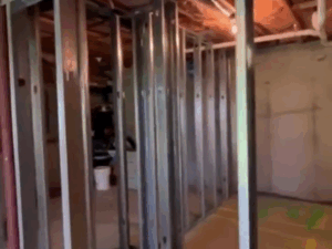 View of a newly installed metal frame basement with steel studs and visible ceiling insulation, showcasing the structural framing process.