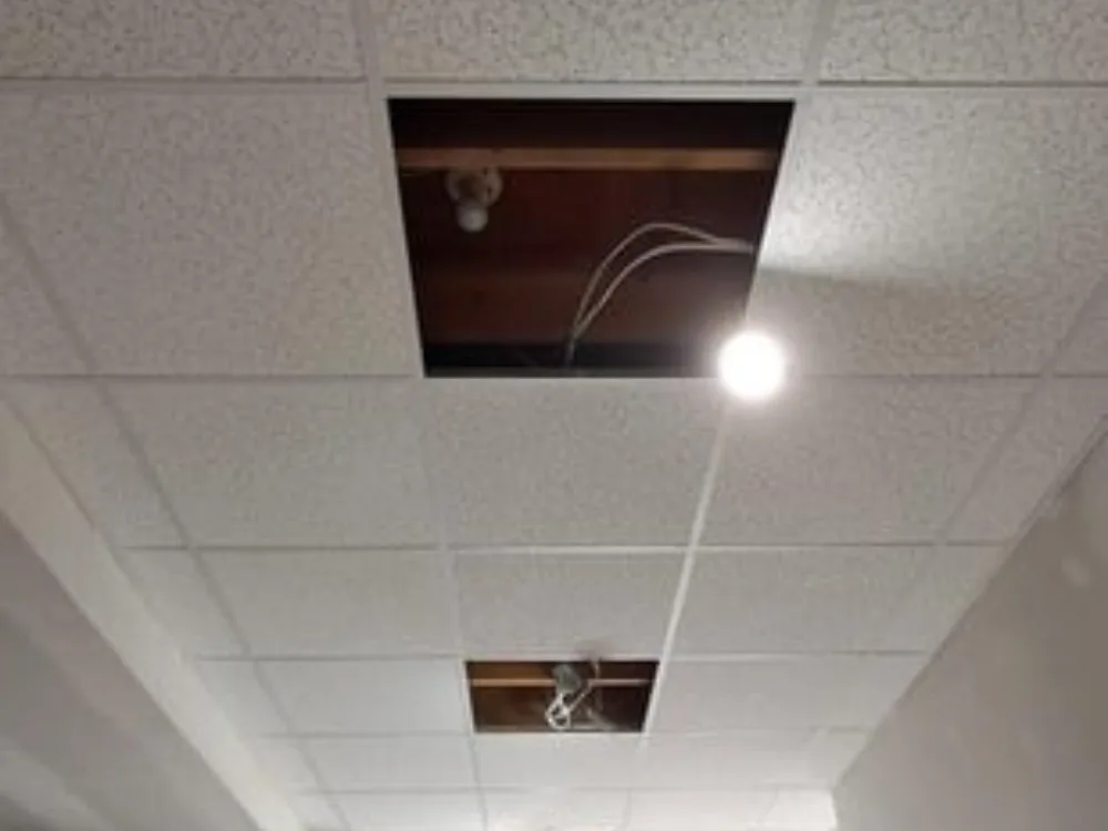 Drop ceiling lighting installation featuring exposed wiring and ceiling access panels.